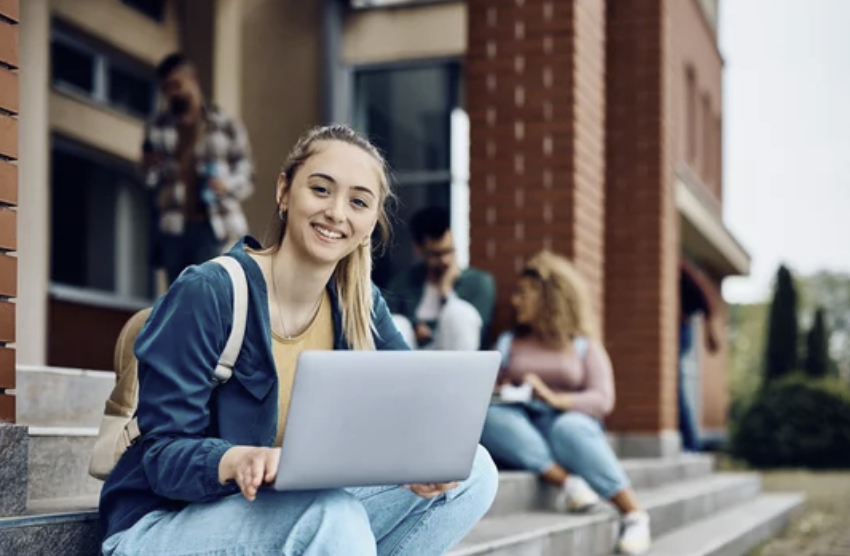 A student using a laptop on the steps outside a building